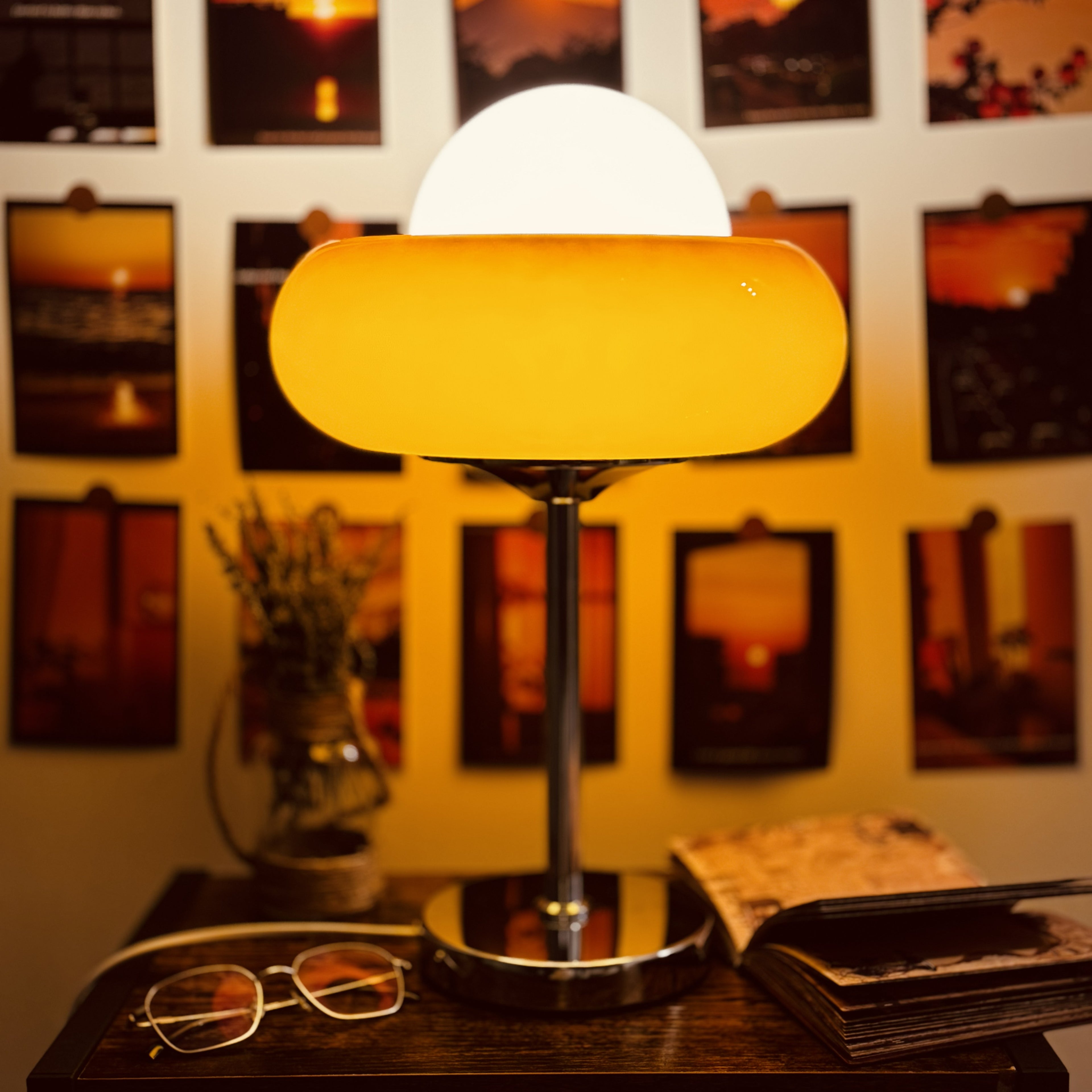 Table lamp with a warm yellow shade on a wooden surface, with blurred artwork in the background.